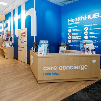 Light wood desk welcoming new patients at the care concierge desk at a CVS Health location. Walls are bright blue with painted white words HealthHub.