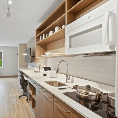 Expansive kitchen in a guest room of an Extended Stay America Hotel, focusing on a white countertop and microwave with a glass-top cook surface.