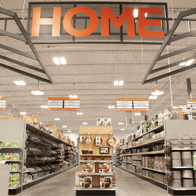 Large orange sign reading 'Home' hanging above aisles of pots, pans and home goods in a remodeled Mills Fleet Farm store.