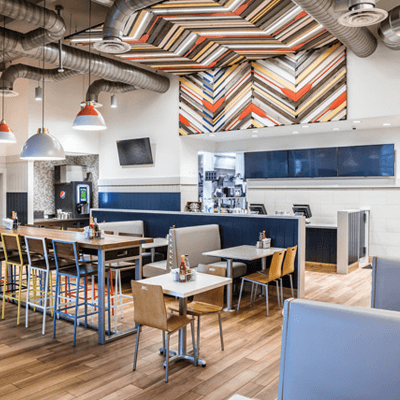 Colorful dining section of a Long John Silver's restaurant, with multi-colored artwork, rainbow-colored metal chairs and rustic wooden flooring.