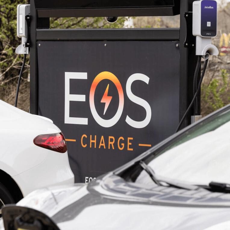 EOS black charging sign next to electrical vehicles in a parking lot. Showcasing newly-installed charging kiosks.