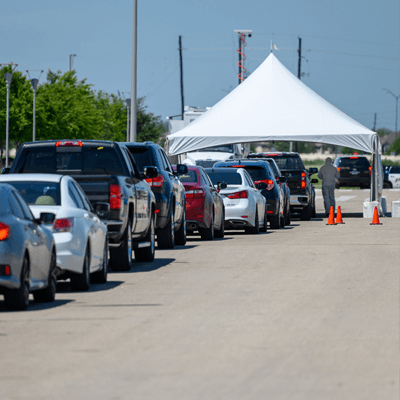 Row of vehicles waiting to enter a white tent, the entrance of the TDEM Covid-19 testing site, managed by DAVACO.