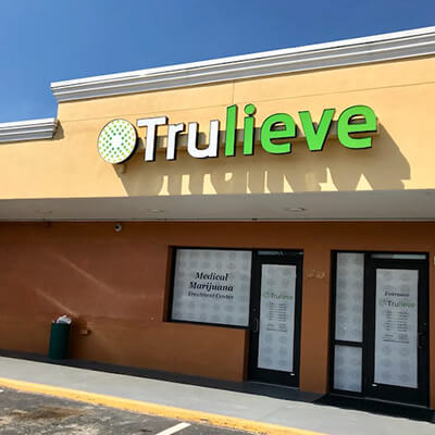 Storefront of a Trulieve cannabis store. The white and green logo sits atop an adobe-style building with glass doors.