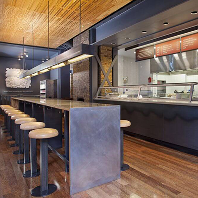 Modern, re-designed Chipotle kitchen and prep station with lighted displays and steel dining tables.